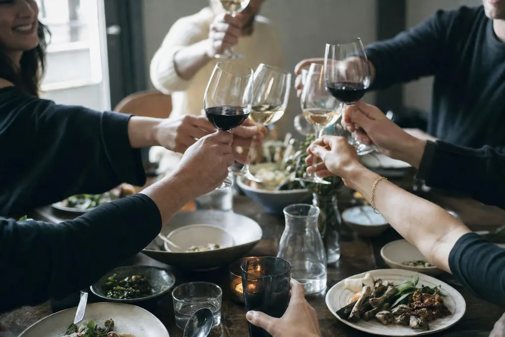 Several hands raising glasses in a toast over a laden dinner table in the evening